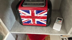 A compact kitchenette with a toaster, a red colander, and a small white appliance on the countertop.