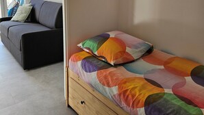 A bedroom with a bed, a wooden nightstand, a grey sofa, and a large mirror.
