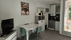 A compact kitchen with a microwave, kettle, and coffee machine. There is a dining table with chairs and a TV on a stand.