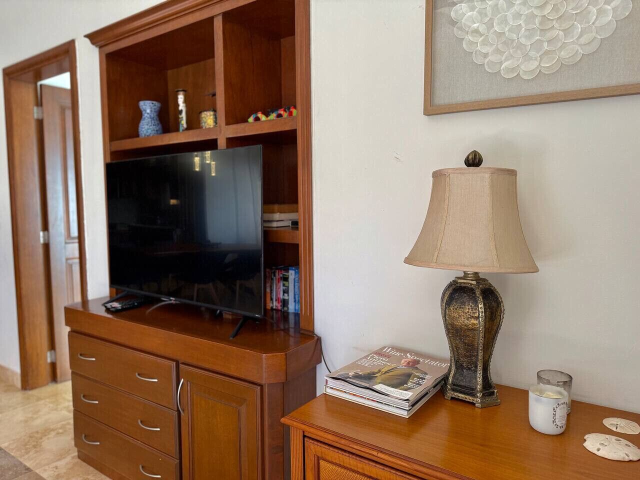 A wooden entertainment center with a flat-screen TV, a lamp, and a magazine on a wooden side table.