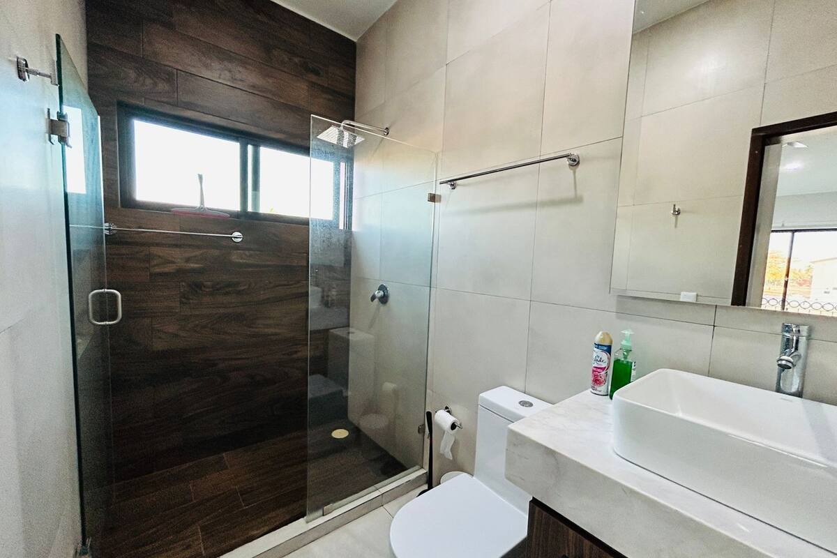 Un baño moderno con ducha envuelta en vidrio, inodoro blanco y un lavabo grande con espejo arriba.