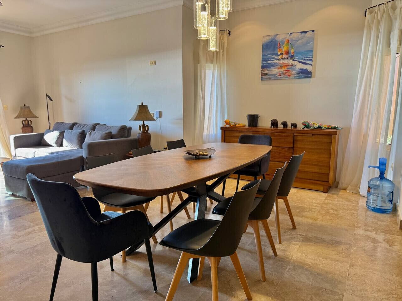 A dining area with a wooden table and black chairs, a sofa, a lamp, and a painting on the wall.