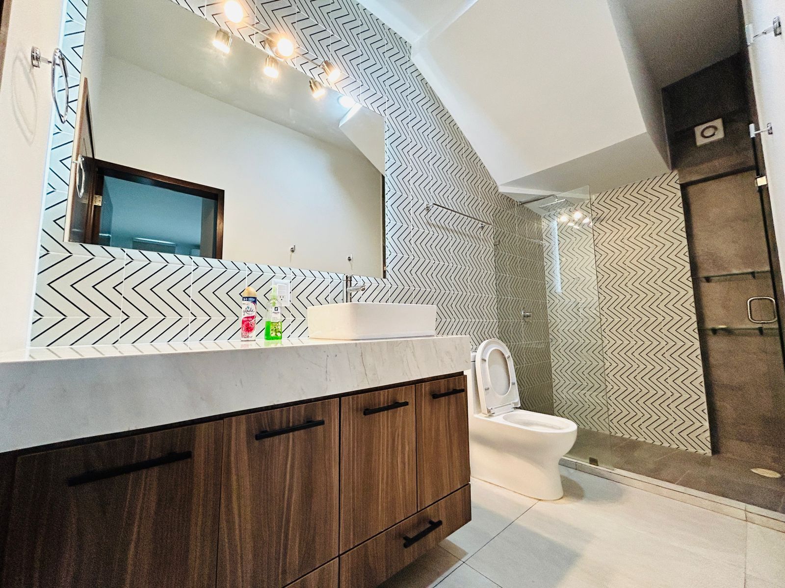 A modern bathroom with a large mirror, a sink, and a toilet.