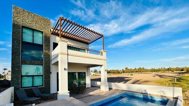 Una casa moderna de dos pisos con piscina, ventanas amplias y un balcón.