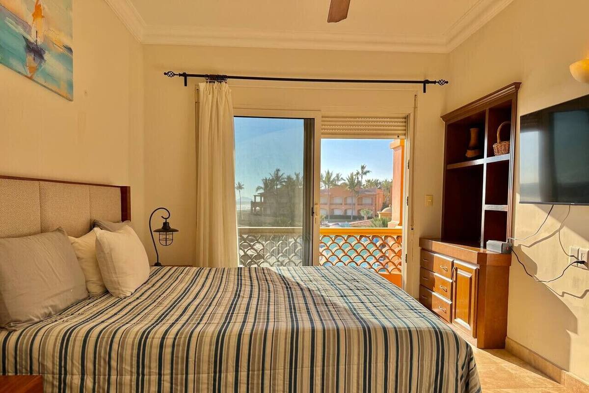 Un dormitorio con una cama grande, un televisor, un armario y un balcón con vistas a palmeras.