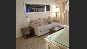 Ein Hotelzimmer mit einer Couch, einem Glastisch, einer Lampe und einem gerahmten Bild an der Wand.