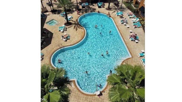 Ein großer, unregelmäßig geformter Pool, umgeben von Liegestühlen und Palmen.