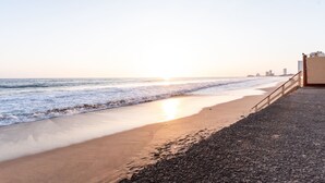 A beach with a pebbly path leading to a building with a balcony overlooking the ocean. - Marina del Rey (Mazatlán)