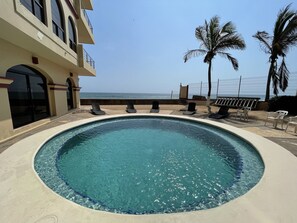 Una piscina con sillones de descanso, vista al océano y palmeras.