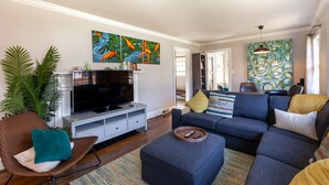 Een moderne woonkamer met een flatscreen televisie, een bank, een bijzettafeltje en een grote plant.