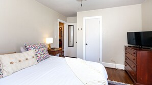 Een slaapkamer met een bed, een dressoir, een televisie en een deur naar een andere kamer.