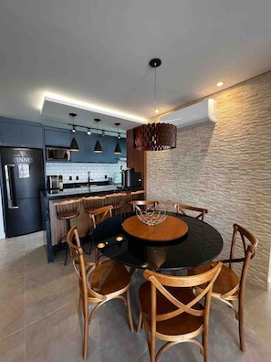 A modern kitchen with a central island, pendant lighting, and a dining area with a round table and wooden chairs.