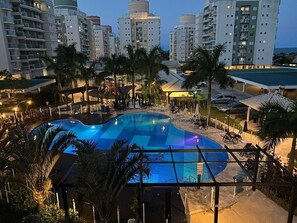 A swimming pool with lounge chairs and palm trees, surrounded by high-rise buildings.