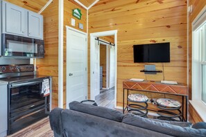 A compact kitchen with a microwave, oven, and a flat-screen TV mounted on the wall.