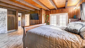 Une chambre spacieuse avec un grand lit, des poutres apparentes en bois au plafond et un téléviseur fixé au mur.