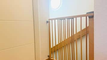 Un escalier en bois avec une rampe en métal, des murs blancs et un luminaire circulaire fixé au mur.