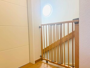 A wooden staircase with a metal railing, white walls, and a circular light fixture on the wall. - Margaretha Vacation Home (Varel)
