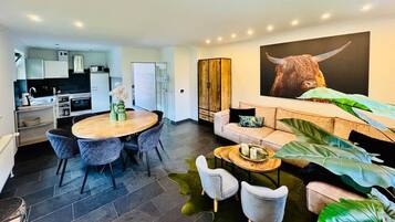 A modern living room with a round wooden table, grey upholstered chairs, a sofa, and a large plant.