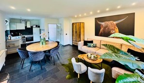 A modern living room with a round wooden table, grey upholstered chairs, a sofa, and a large plant. - Margaretha Vacation Home (Varel)