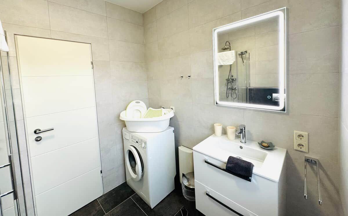 Ein kleines Badezimmer mit Waschmaschine, Waschbecken und Spiegel sowie einer Tür.