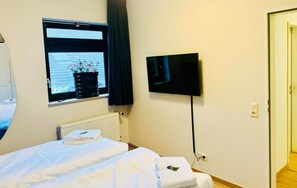A hotel room with a bed, a window with a view, a television, and a radiator. - Margaretha Vacation Home (Varel)