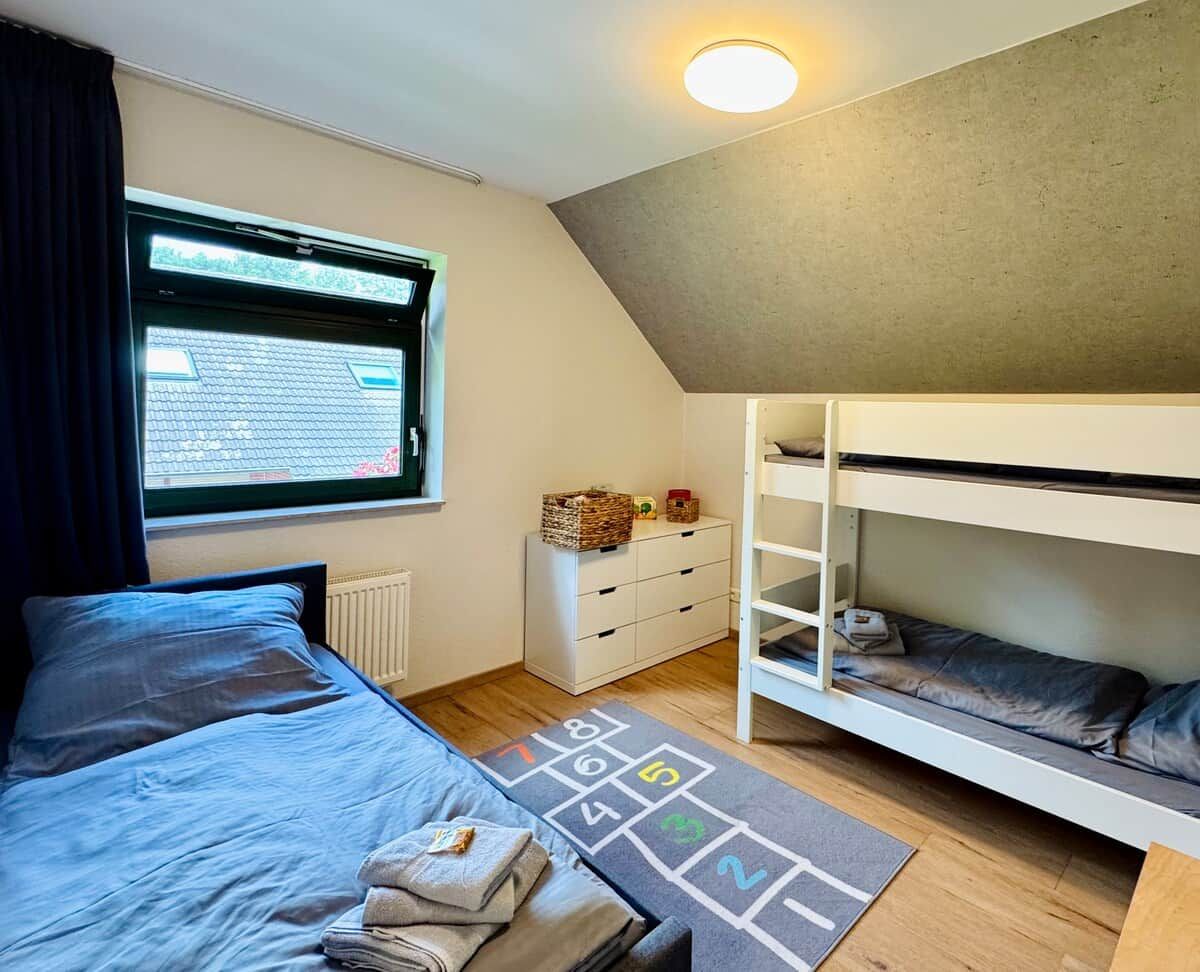 A bedroom with a bunk bed, a window with a view, a heater, a dresser, and a play mat.