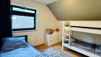Une chambre avec un lit superposé, une fenêtre donnant sur un paysage agréable, un radiateur, une commode et un tapis de jeu.