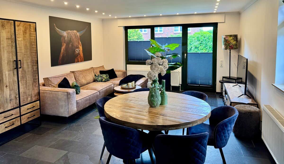 Ein modernes Wohnzimmer mit einer Couch, einem runden Holztisch und einem großen Fenster.