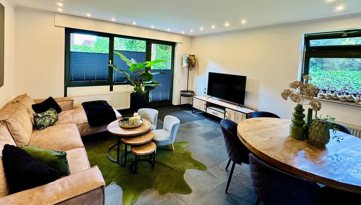 Ein modernes Wohnzimmer mit einer Couch, Sesseln, einem Couchtisch und einem Fernseher.