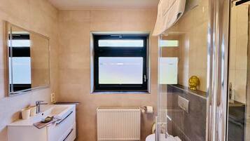 Une salle de bain avec un lavabo blanc, un miroir, une fenêtre, des toilettes et une douche.