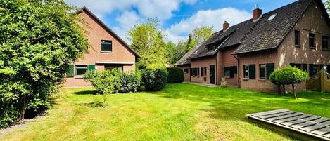 A residential property with a well-maintained lawn, a wooden deck, and brick houses with multiple chimneys.