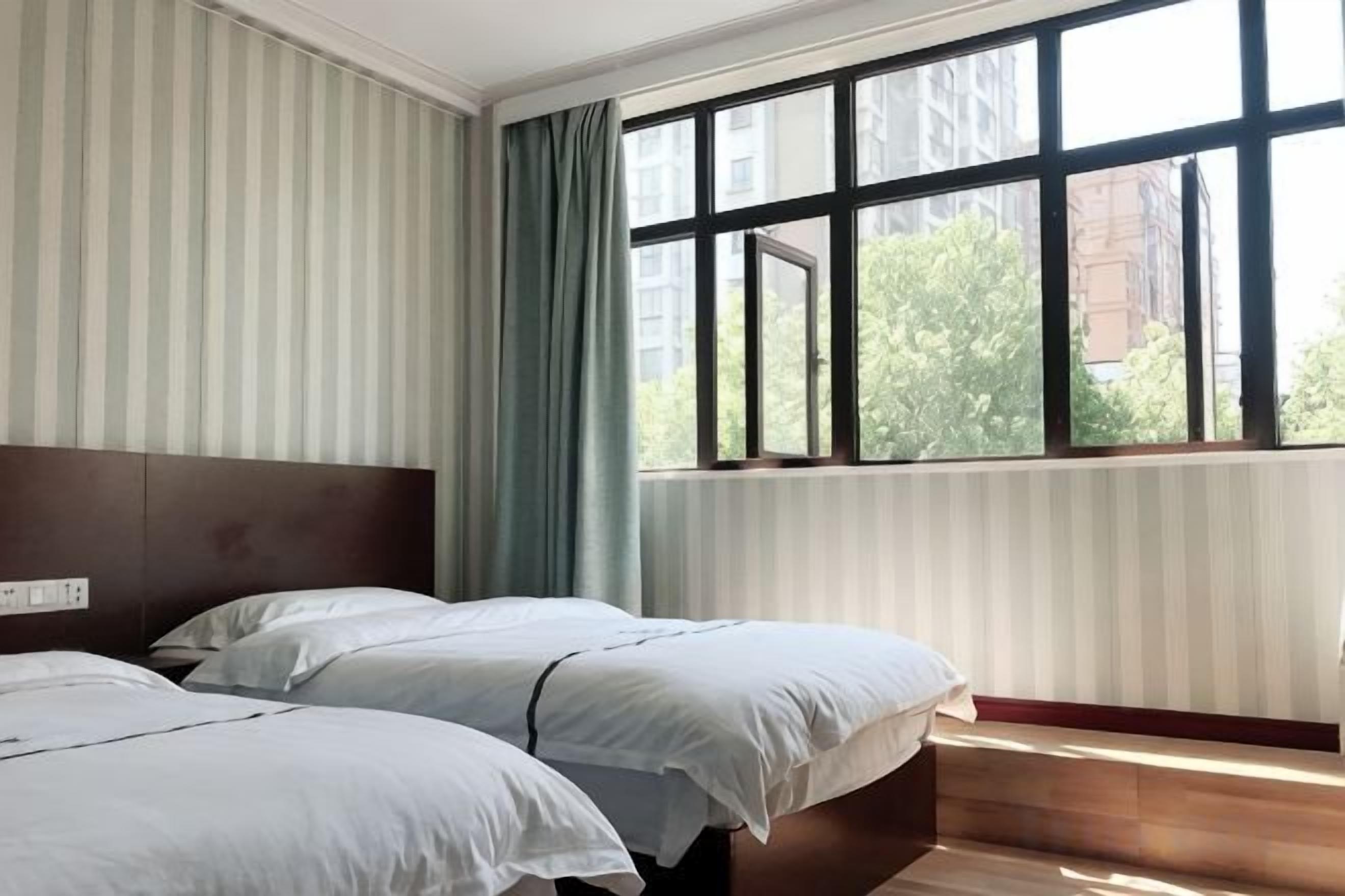 A hotel room with two beds, a window with curtains, and a view of buildings outside.