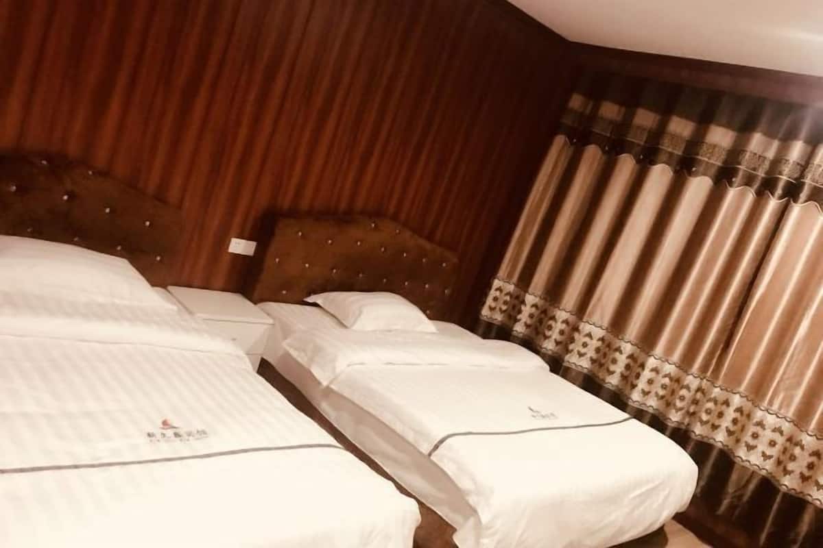 Habitación de hotel con dos camas, cabeceros de madera y cortina con borde estampado.