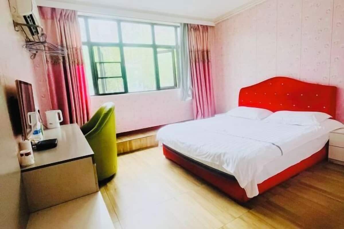 Habitación de hotel con cama, escritorio, silla, ventana con cortinas y estante en la pared.
