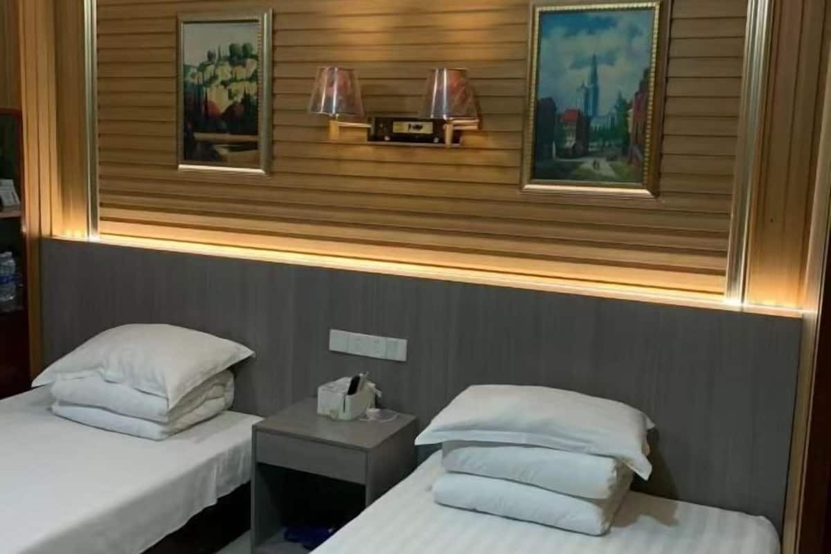 Habitación de hotel con dos camas, una mesita de noche, una lámpara y dos cuadros en la pared.