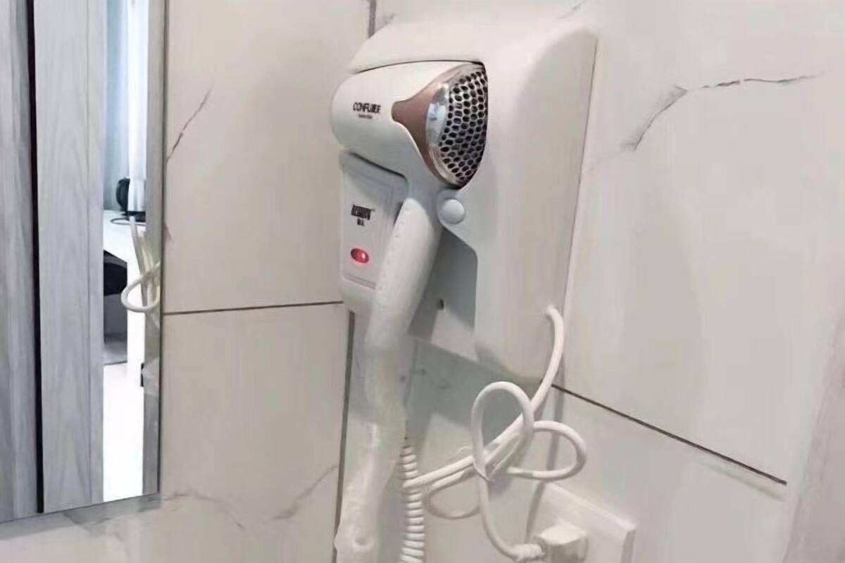 Un secador de pelo sujeto a la pared, un enchufe y una grieta visible en la pared.