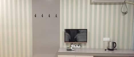 A room with a striped wall, a flat-screen TV, a white cabinet, and a wall-mounted air conditioner.