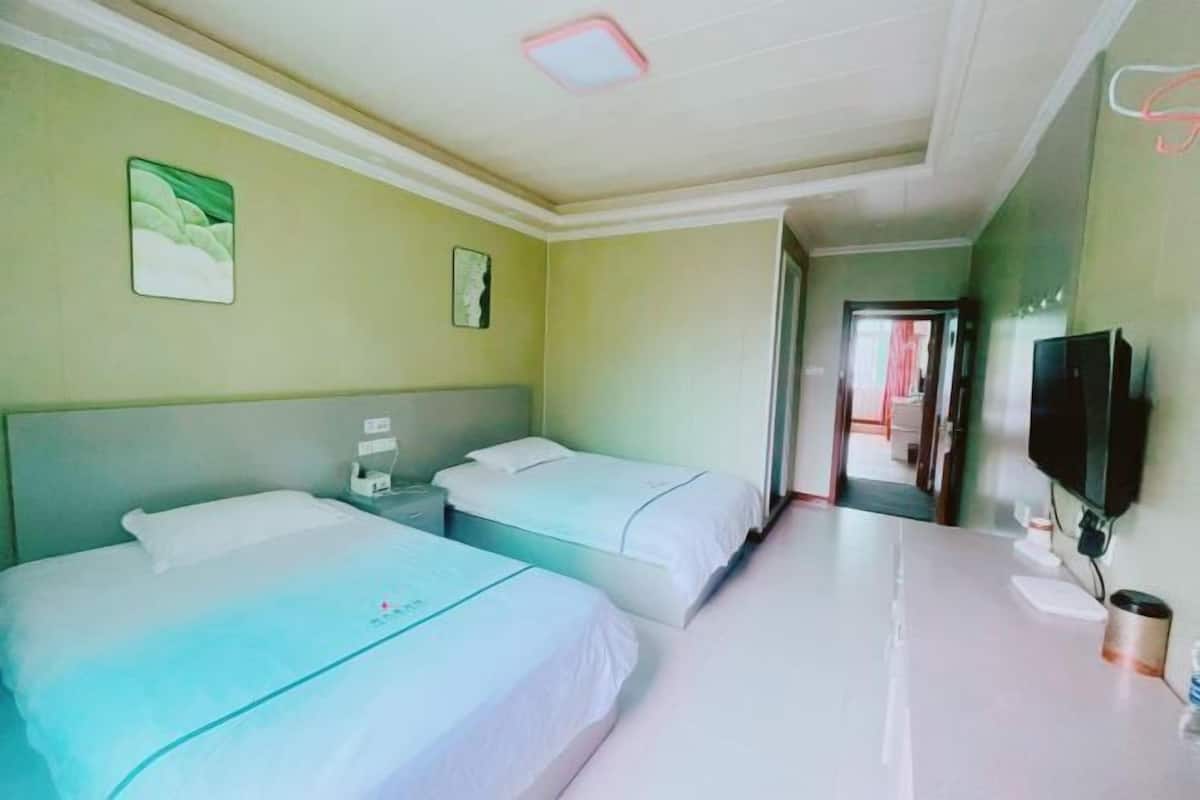 Habitación de hotel con dos camas, un televisor, una mesita de noche y una puerta que da a otra habitación.