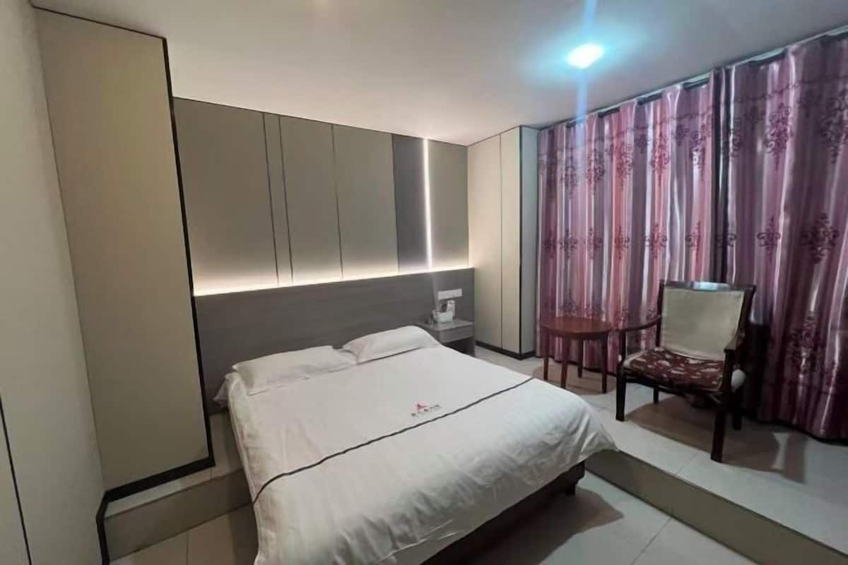 Habitación de hotel con cama, mesita de noche, silla y cortina.
