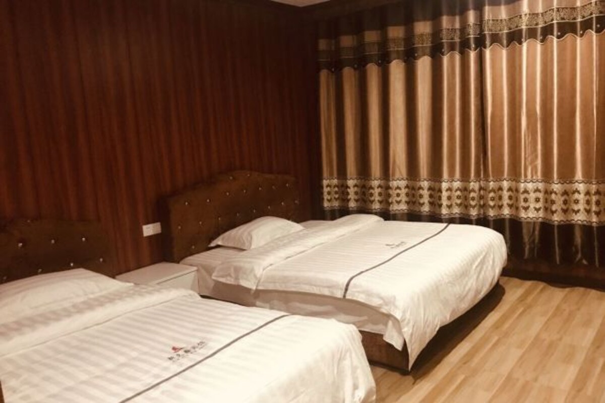 Habitación de hotel con dos camas, cabecero de madera y un ventanal con cortinas.