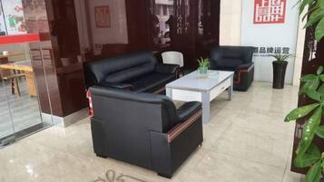 A hotel lobby with a black leather sofa, a white coffee table, and a black armchair. There is a potted plant on the coffee table and a red sign on the wall.