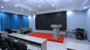 Un salón de conferencias con escenario, atril y proyector.