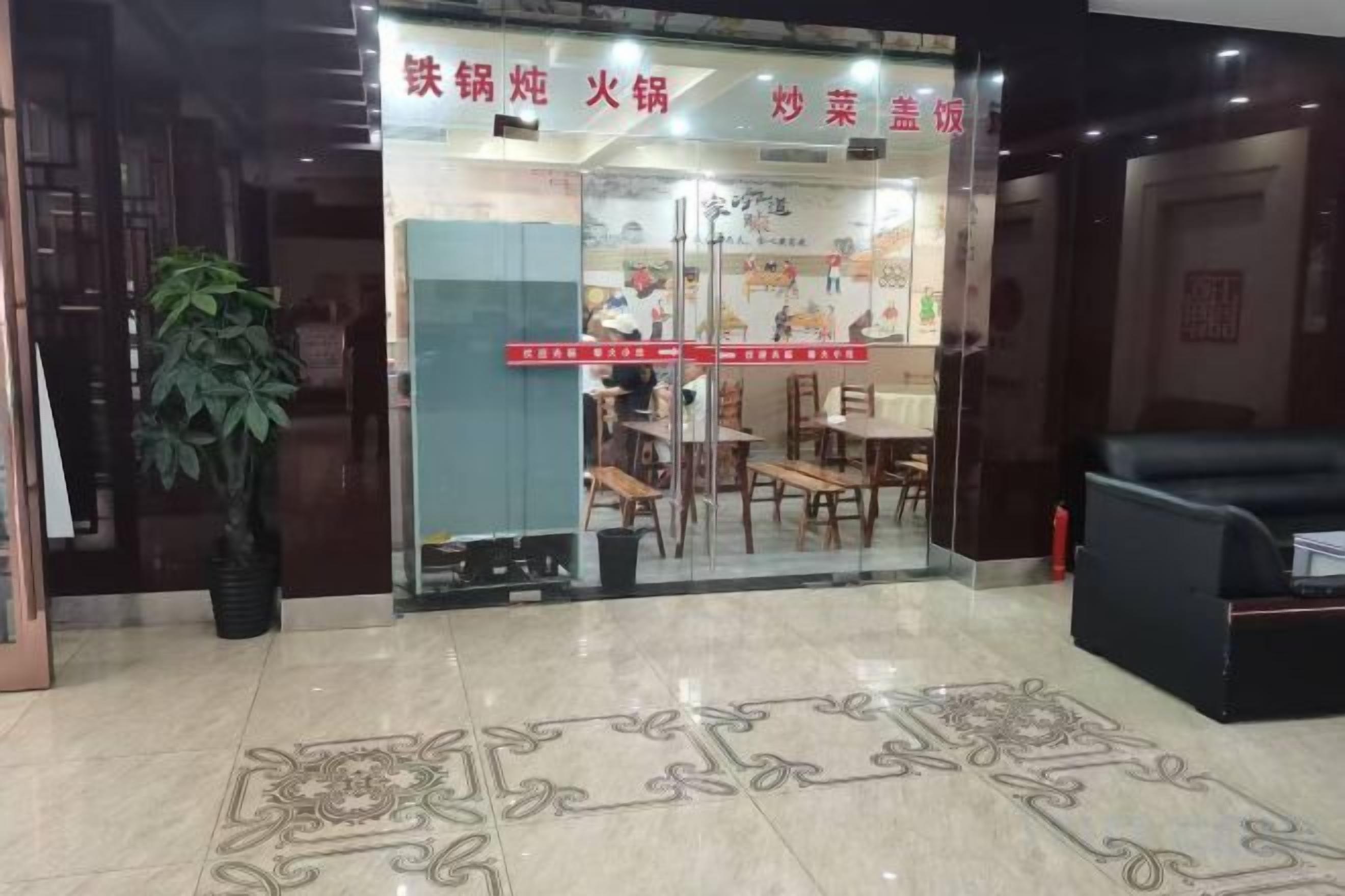 A restaurant entrance with a glass door, indoor seating, and a potted plant outside.