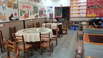 Interior de restaurante con mesas redondas, sillas de madera y una pizarra con el menú.