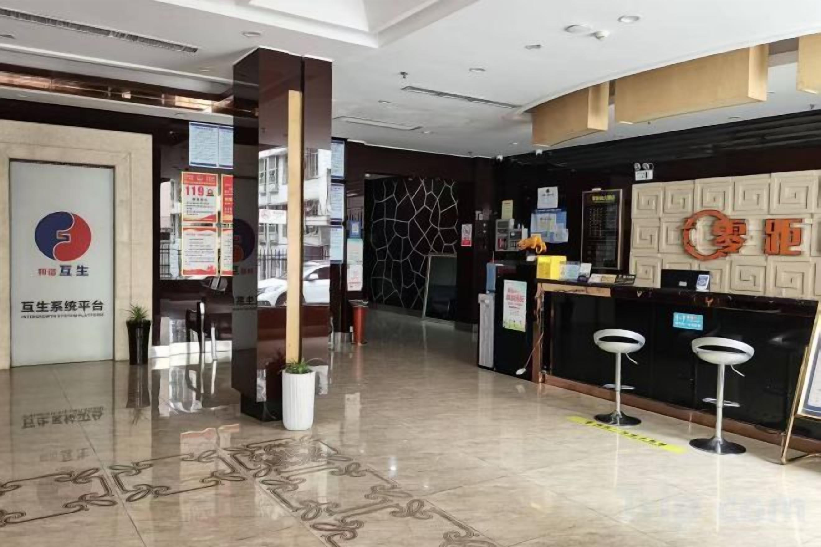 Zona de recepción de un hotel con mostrador, taburetes de bar y una planta en maceta.