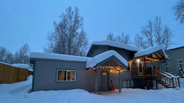 A snow-covered house with a porch, a staircase, and string lights. - Alaskan studio in the mountains (Anchorage)