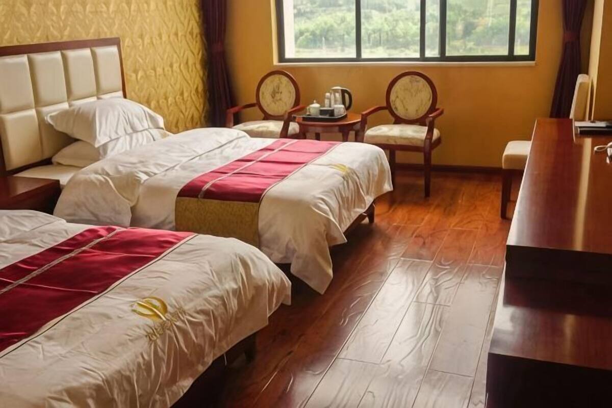 A hotel room with two beds, wooden flooring, a window with a view, and a desk with a chair.