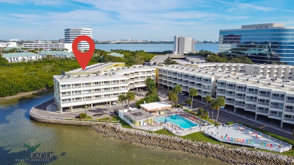 A multi-story hotel with a pool and outdoor seating area, surrounded by greenery and a body of water. - Water View*Ideal Location*Pool (Tampa)