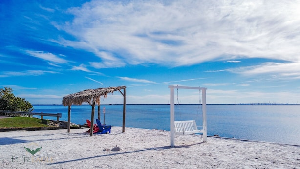 Una playa con un columpio, una estructura de paja y un banco.