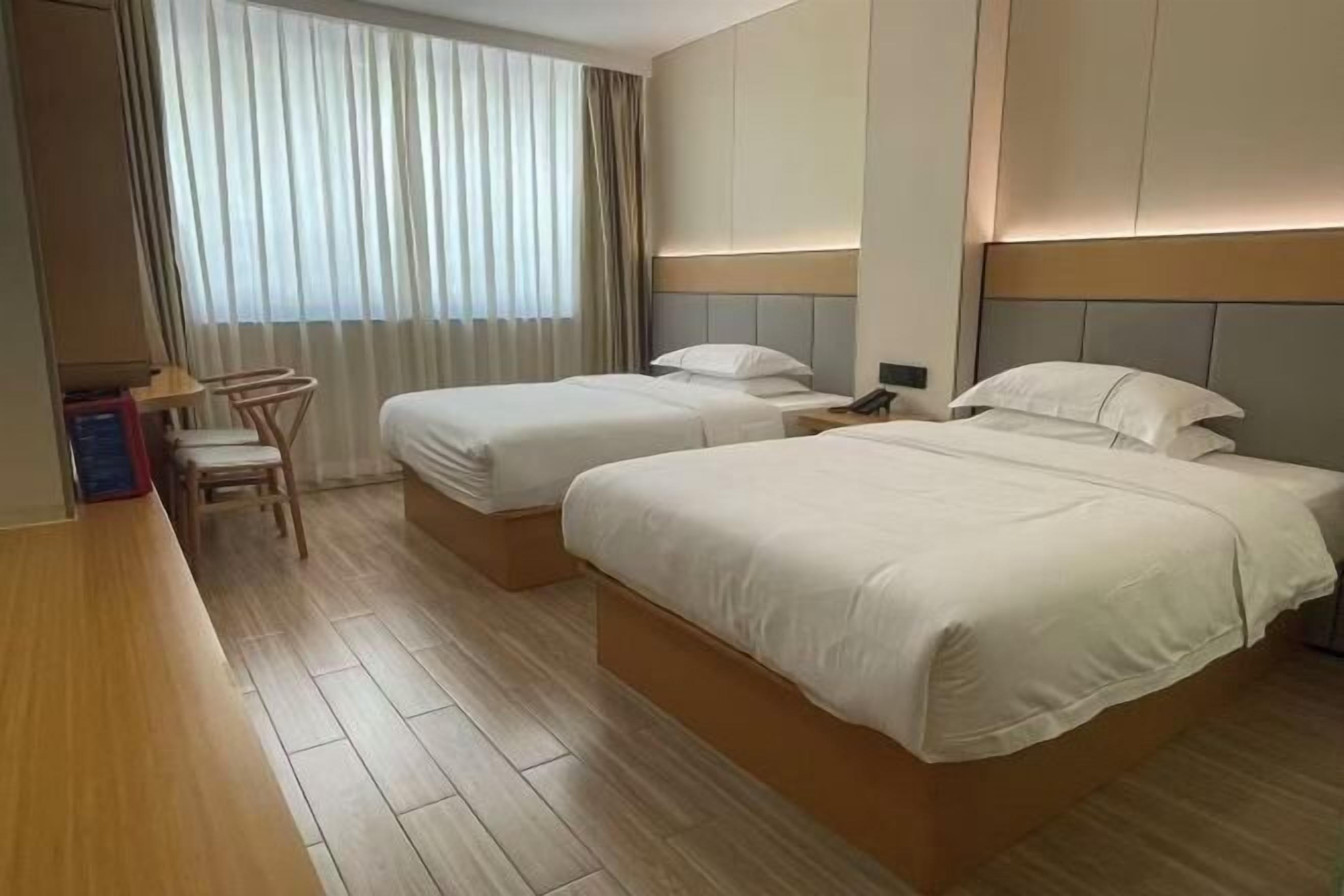 Una camera d'albergo con due letti, una scrivania, una sedia e una finestra con tende.